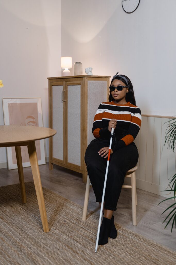 Blind Woman with Sunglasses Sitting on a Chair and Holding a White Cane